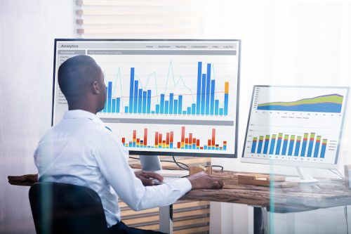 Rear View Of Young Businessman Looking At Graph On The Computers In The Office